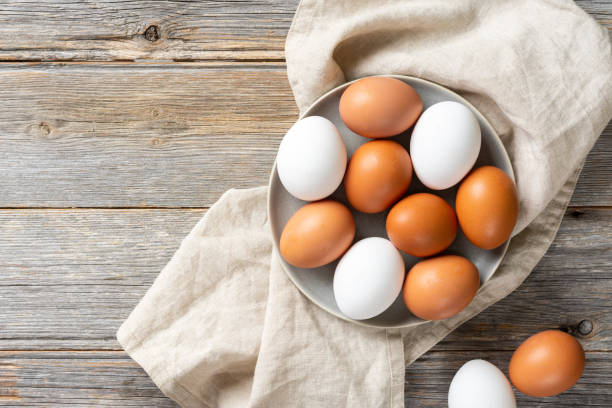 istock Eggs in a plate on the kitchen table. White and brown eggs for cooking. Chicken eggs on a wooden culinary background. Concept of preparation for baking. Top view with space for text 1253809506