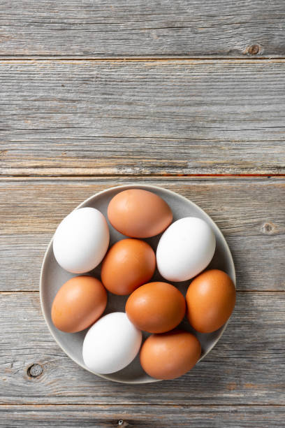 istock Eggs in a plate on the kitchen table. White and brown eggs for cooking. Chicken eggs on a wooden culinary background. Concept of preparation for baking. Top view with space for text 1253809655