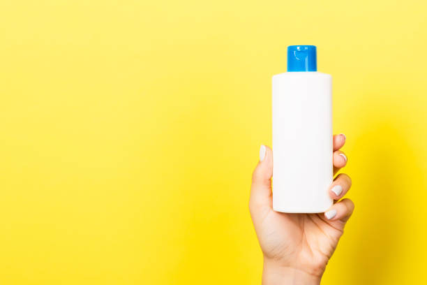 istock Yellow background with woman's hand holding a cosmetics bottle with copy space 1253810609