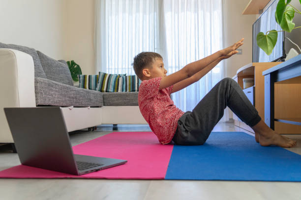 ラップトップコンピュータを持つティーンエイジャーの少年は、リビングルームでヨガを練習し、スポーツエクササイズをしています。スポーツ、健康的なライフスタイル、自宅でのアクテ� - living room learning healthy lifestyle one person ストックフォトと画像