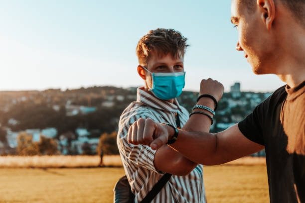 junge männer ellenbogen bump trägt corona virus schutzgesichtsmasken - greeting teenager handshake men stock-fotos und bilder