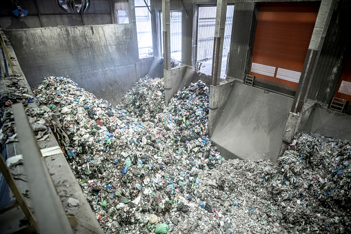 High angle view of large indoor waste management facility and mechanical grabber in use transferring potential recyclables.