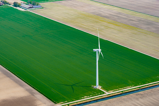 Aerial view of a wind turbine in Flevoland standing in between   fields growing crops in spring The Netherlands.