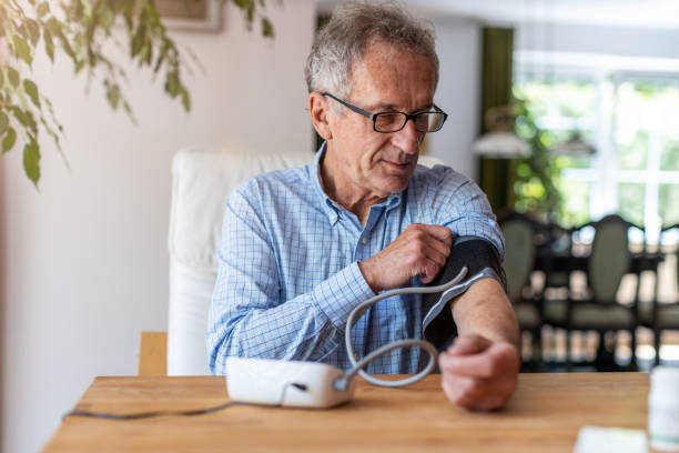 hombre de la tercera edad usando un dispositivo médico para medir la presión arterial - hipertension fotografías e imágenes de stock