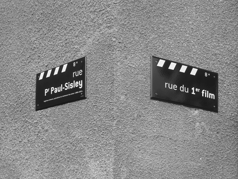 This is a street sign for the street where the very first moving picture image was created by the Lumiere brothers. As it literally translates 'Road of the first film'. It is on the corner with the street named after Professor Paul Sisley who invented a process protecting fabrics from developing red spots.
