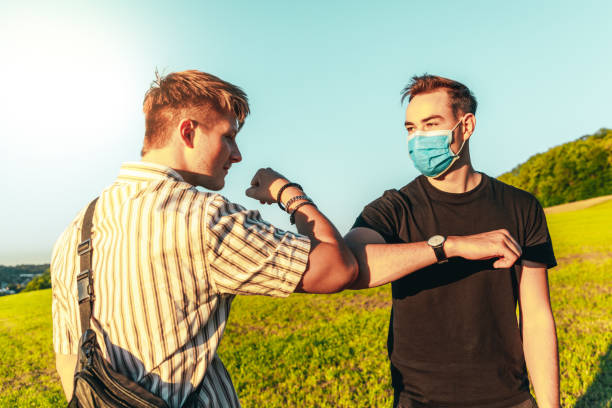 ellenbogen bump freunde gruß mit schützenden gesichtsmasken - greeting teenager handshake men stock-fotos und bilder