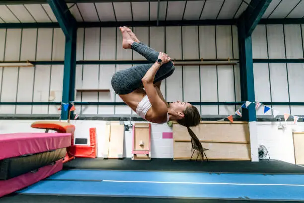 Photo of Fit female athlete in early 30s practicing flip in gym