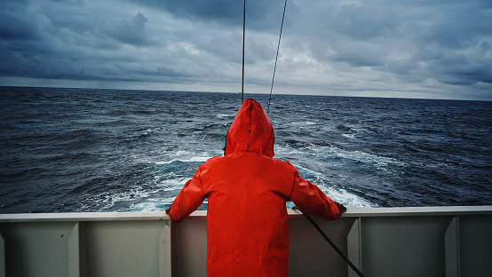 Fisherman staring at sea on the fishing boat deck, with a orange raincoat