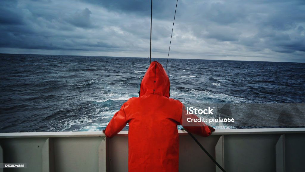 Fisherman staring at sea on the fishing boat deck, with a orange raincoat Fisherman Stock Photo