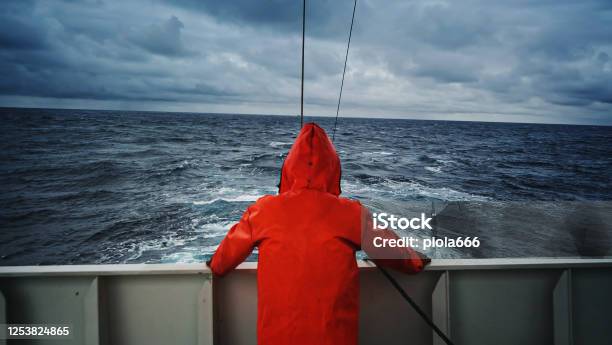 Fisherman Staring At Sea On The Fishing Boat Deck With A Orange Raincoat Stock Photo - Download Image Now