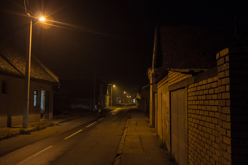 picture of a deserted empty rural dark road, with bad orange public lighting, in a countryside of Europe.