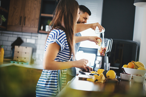 Young couple making healthy drink at their kitchen.