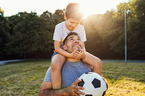 Happy hispanic father play soccer with his cute son.They enjoy in nature and nice summer sunset.