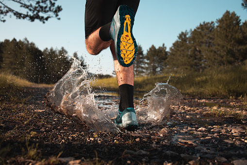 Shot of the legs of a man who is stepping into a puddle while running through the forest.
