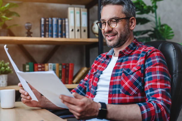 istock Adult male executive checking documents while sitting at his desk in home office 1253833479