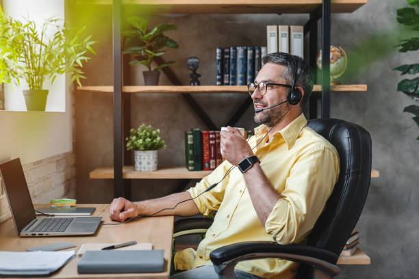 Man in headset having break and drinking coffee while working at home Man in headset having break and drinking coffee while working at home home office photos stock pictures, royalty-free photos & images