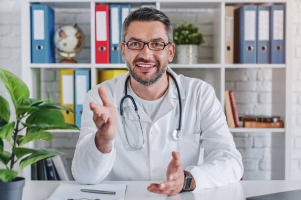 istock Senior doctor talking to camera in video chat from his office 1253833610