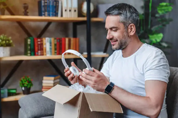 Photo of Joyful middle aged man get his delivery with heaphones at home