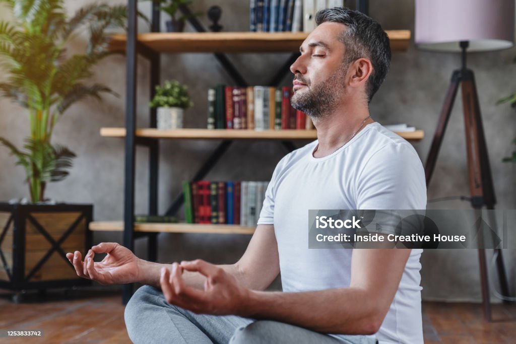 Middle aged man meditating at his living room floor sitting Men Stock Photo