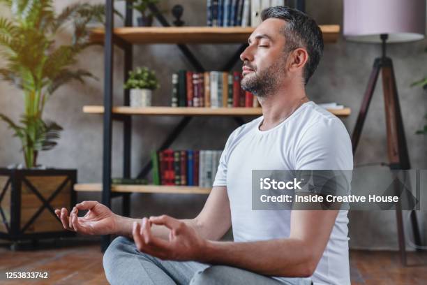 Middle Aged Man Meditating At His Living Room Floor Sitting Stock Photo - Download Image Now