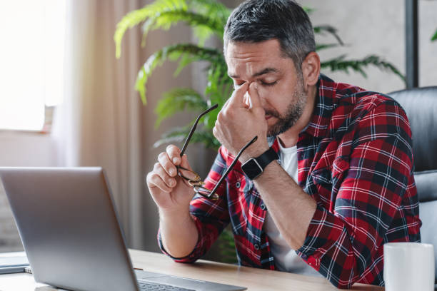 hombre caucásico cansado sufren de dolor de cabeza problema de visión mala sentado en la mesa de casa usando portátil - tired man fotografías e imágenes de stock