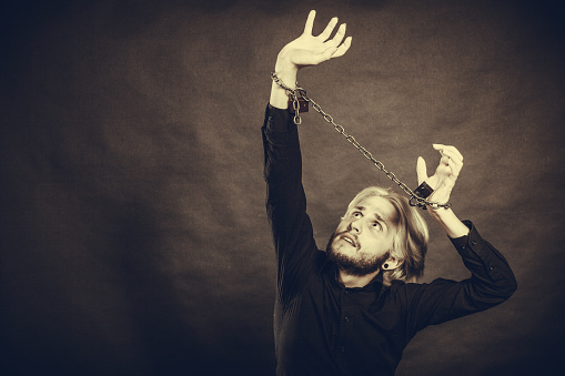 No freedom, social problems concept. Sad man with chained hands, studio shot on dark grunge background