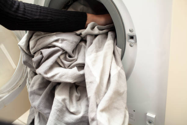 Close-up of bed sheets being loaded into washing machine Close-up of hands loading bed sheets into a washing machine bedding stock pictures, royalty-free photos & images