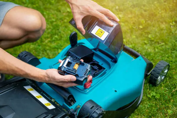 Photo of man putting battery into electric cordless lawn mower