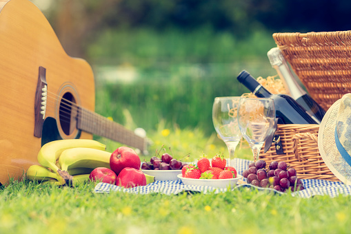 Picnic setting with red wine, glasses, bottle, picnic hamper basket, guitar and food ready for party