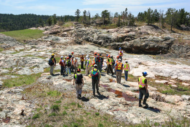 Group of workers and geologists in hardhats and high-visibility vests standing on geological outcrop site. SUDBURY, ONTARIO, CANADA - MAY 21 2009: Group of workers and geologists in hardhats and high visible vests inspecting site. View from the back. Gathering on rock formation. geologist stock pictures, royalty-free photos & images
