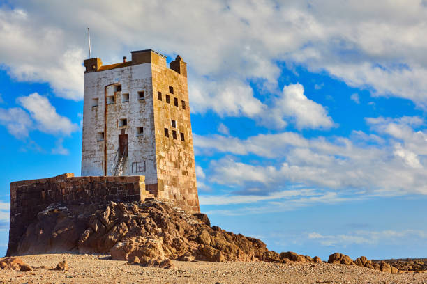 Image of Seymour Tower at low tide with stones, cloudy sky and sunshine.