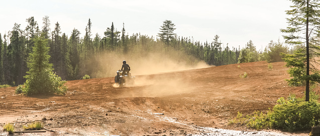 Man driving ATV quad in sandy terrain with high speed. Trail of dust behind the biker.