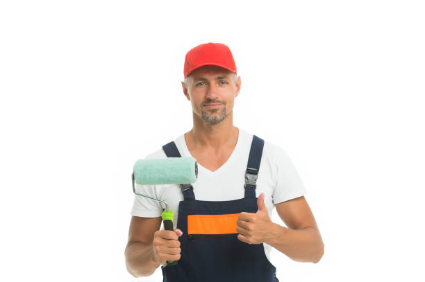 istock Interior Color Trends. Paint rolling. Decorator hold paint roller. Wall painter. Paint work. Paint shop. Renovation and repair. Renewal and redecorating. Professional equipment. Mature man in cap 1253855038