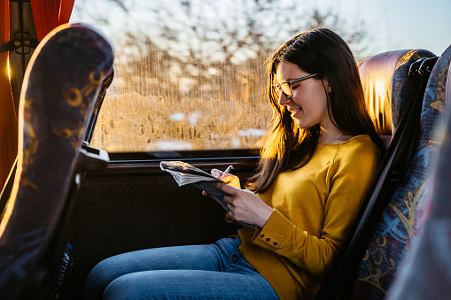 Young beautiful Caucasian woman solving crosswords in bus on a road trip.