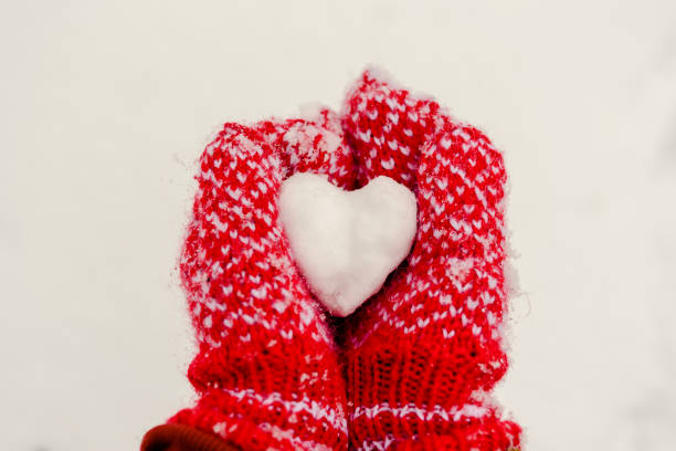 istock Heart shaped snowball in hands in knitted mittens 1253859428