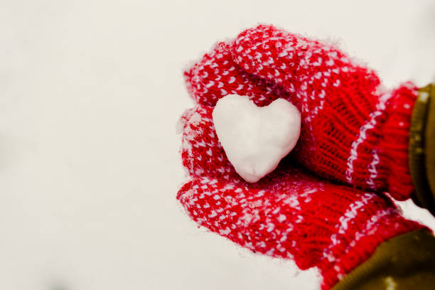 istock Heart shaped snowball in hands in knitted mittens 1253859455