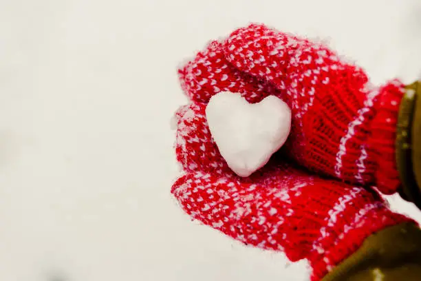 Heart shaped snowball in hands in red knitted mittens