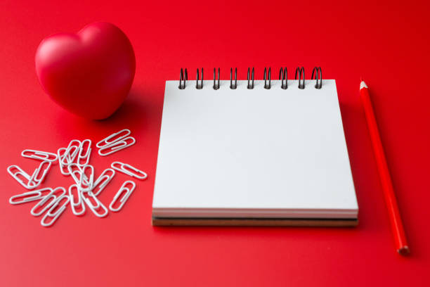 istock Notebook, pencil, paper clip, heart shaped ball on a red background and copy space 1253860274