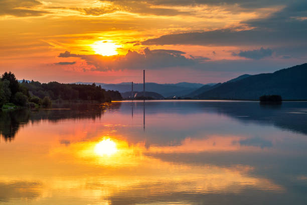 Industrial landscape with chimney constructions reflected on the water surface of the dam at sunset. Zilina dam in the north of Slovakia, Europe.