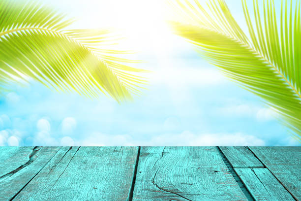 istock Blur tropical beach with bokeh sun light wave and palm tree on copy space empty old wood table abstract background. 1253861036
