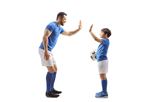 Full length profile shot of an adult football player gesturing high five with a junior football player isolated on white background