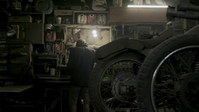 Authentic motorcycle master works as a grinder in an old workshop against a background of vintage motorcycles