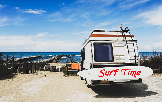 Rear view of vintage camper parked on the  beach against a beautiful scenic view - Caravan of surfer with a surfboard on back - Nomadic life concept of surfer waiting for better waves - Surf Time text