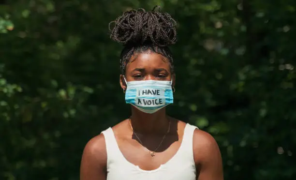 A young woman wears a face mask during global pandemic that says "I have a voice."