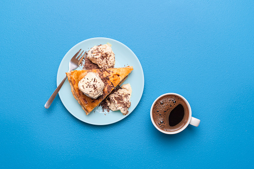 Apple pie slice with golden crust served with vanilla ice cream and a hot coffee on a blue table. Flat lay with an apple tart. Thanksgiving dessert.