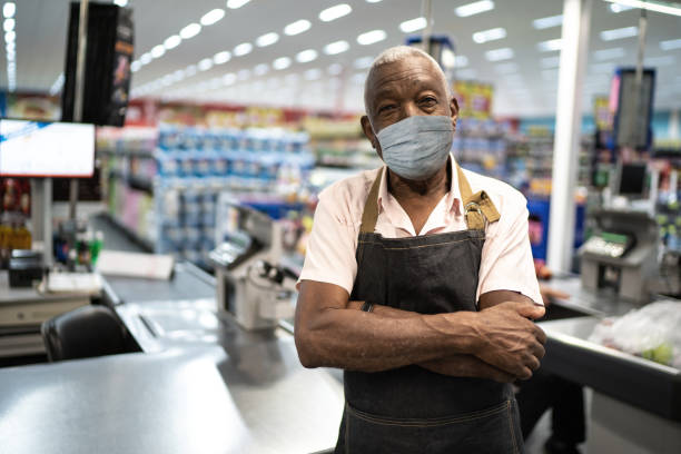 Afro senior man business owner / employee with face mask at supermarket Afro senior man business owner / employee with face mask at supermarket reopening photos stock pictures, royalty-free photos & images