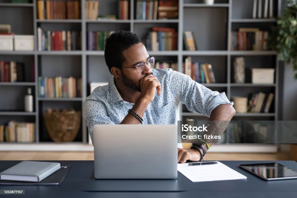 Afrikanischer Geschäftsmann, der am Arbeitsplatz sitzt und über Problemlösung nachdenkt - Lizenzfrei Betrachtung Stock-Foto