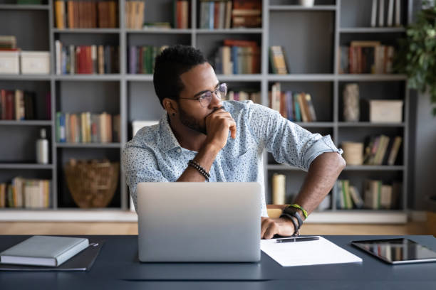 uomo d'affari africano seduto sul posto di lavoro pensando alla soluzione del problema - decidere foto e immagini stock