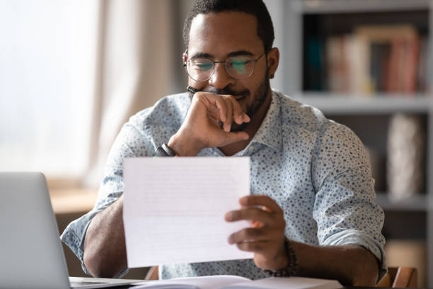 istock African man sitting at desk reading letter feels satisfied 1253877197
