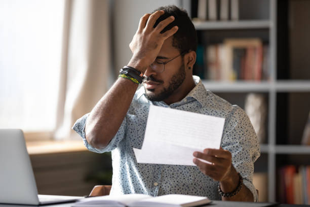 afrikaanse zakenman die brief houdt die slecht banknieuws over schuld leest - ongebruikelijk stockfoto's en -beelden